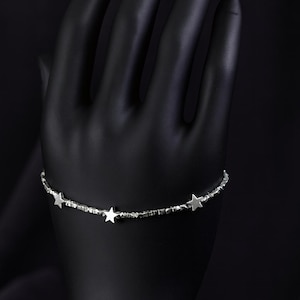 May include: A silver bracelet featuring three star-shaped charms. The bracelet is presented against a black backdrop. The stars are evenly spaced along the bracelet's length, creating a celestial theme.
