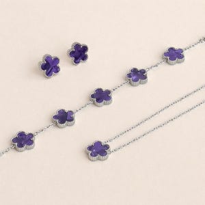 May include: A jewelry set featuring a necklace, bracelet, and stud earrings. Each piece has a silver-colored metal setting with a four-leaf clover design. The clovers are filled with a deep purple material, creating a striking contrast.