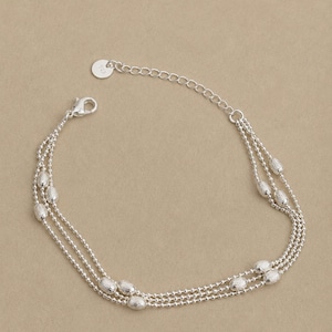 May include: A silver-toned multi-strand bracelet featuring three delicate ball chains interspersed with small, textured oval beads. The bracelet includes a lobster claw clasp, an adjustable extender chain, and a small round tag stamped with 925.