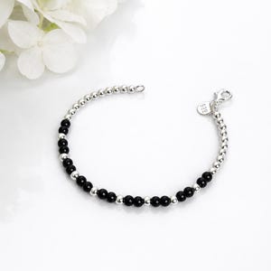 May include: A beaded bracelet featuring alternating small polished silver spheres and smooth black round beads. The bracelet includes a silver lobster claw clasp and a small circular tag stamped with the number 925, indicating sterling silver.