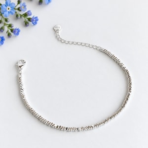 May include: A silver-coloured bracelet composed of numerous small, faceted metallic beads. The bracelet features a lobster claw clasp and an adjustable extender chain with a small heart-shaped charm stamped with the number 925.