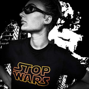 May include: Black t-shirt with the words "STOP WARS" in a yellow and orange gradient font. The image is a black and white photo with a person wearing sunglasses and a black shirt. The background has a white and black graphic design.