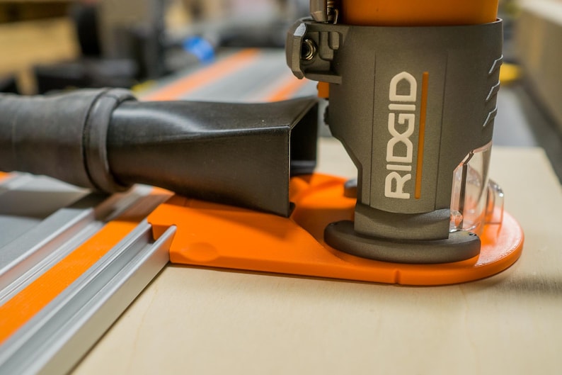 May include: Close-up of a gray and orange RIDGID power tool. The tool has a black hose attached and is mounted on an orange base. The word "RIDGID" is printed in white on the side of the tool.