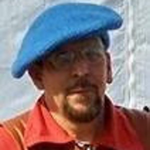 May include: A vibrant blue beret, crafted from a soft fabric, is worn on a person's head. The beret is tilted to one side. The person is wearing a red collared shirt.