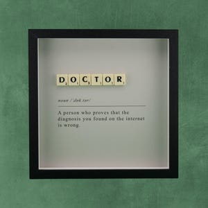 Op de afbeelding: Een ingelijst kunstwerk met het woord "DOCTOR" in letters. Hieronder staat de definitie: "Een persoon die bewijst dat de diagnose die je op internet hebt gevonden, verkeerd is."