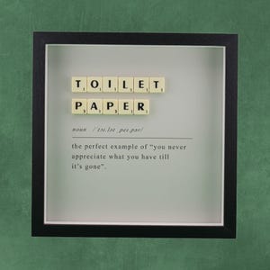 Pode incluir: Uma moldura quadrada preta tipo caixa contendo peças de letras na cor creme que formam a palavra TOILET PAPER. Abaixo das peças, o texto diz: noun /ˈtɔɪ.lət ˌpeɪ.pər/ the perfect example of “you never appreciate what you have till it’s gone”.