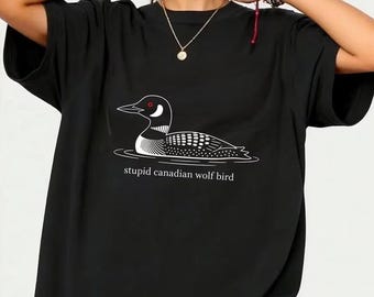May include: Black t-shirt featuring a white graphic of a loon floating on water, with the text "stupid canadian wolf bird" below the image. The design is a simple line drawing style.
