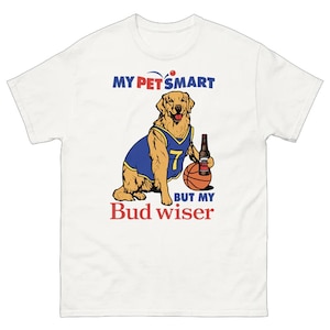 May include: White t-shirt with a graphic of a golden retriever wearing a blue basketball jersey with the number 7, holding a beer bottle and a basketball. Text reads "MY PET SMART BUT MY Bud wiser."