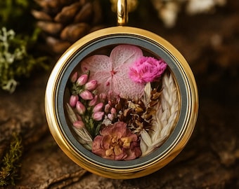 Op de afbeelding: Een goudkleurige, ronde hangerketting met een heldere glazen voorkant, met een delicate opstelling van gedroogde roze en beige bloemen. De hanger hangt aan een gouden lus, tegen een natuurlijke houten achtergrond. Een uniek bloemenaccessoire.