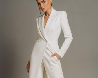 May include: A white, double-breasted jumpsuit with a long, flowing jacket-like top. The pants have a split front design. The model is wearing gold-colored pointed-toe heels. The outfit is a formal, elegant style.