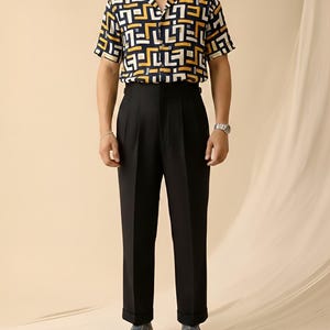 Puede incluir: Una camisa de manga corta con un estampado geom&eacute;trico en azul marino, blanco y amarillo se combina con pantalones negros con pliegues. El conjunto se completa con mocasines de cuero marr&oacute;n.