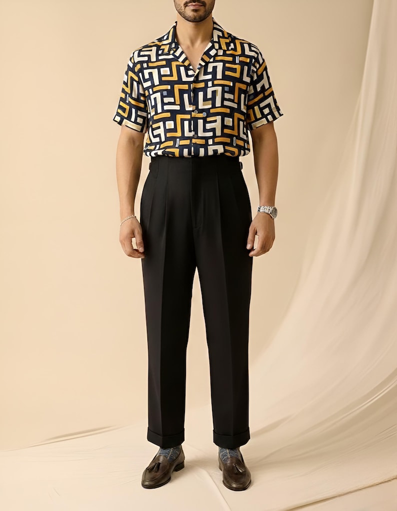Puede incluir: Una camisa de manga corta con un estampado geom&eacute;trico en azul marino, blanco y amarillo se combina con pantalones negros con pliegues. El conjunto se completa con mocasines de cuero marr&oacute;n.