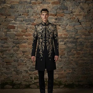 May include: A black coat with gold floral embroidery, paired with black pants and shoes. The coat features intricate detailing and a high collar. A gold headband completes the ensemble. The outfit is formal and elegant.