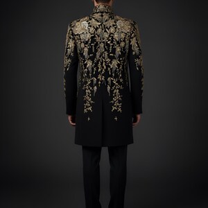 May include: A black formal coat with intricate gold embroidery. The design features floral patterns cascading down the back and sleeves. The coat is paired with black trousers, creating a sophisticated ensemble.