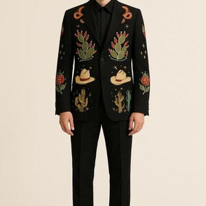 May include: Black suit with embroidered desert-themed designs. The blazer features cacti, cowboy hats, and roses in green, red, and yellow. The suit is paired with a black dress shirt and black dress pants.