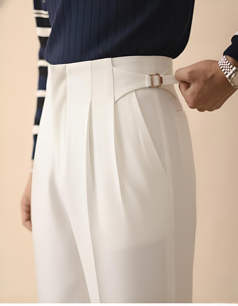 Puede incluir: Primer plano de un pantal&oacute;n blanco plisado con cintura alta y detalle de hebilla. El pantal&oacute;n se combina con un jersey de punto acanalado azul marino. Una mano ajusta la hebilla del pantal&oacute;n.