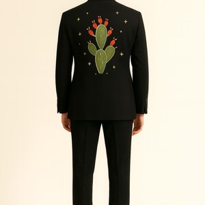 May include: Black suit with an embroidered cactus design on the back. The cactus is green with red accents, surrounded by small gold stars. The suit includes a matching black jacket and pants.