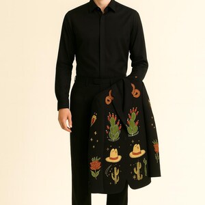 May include: A person wearing a black button-down shirt and black pants, holding a black jacket. The jacket is decorated with colorful embroidered cacti, hats, and flowers. The overall theme is Western-inspired apparel.