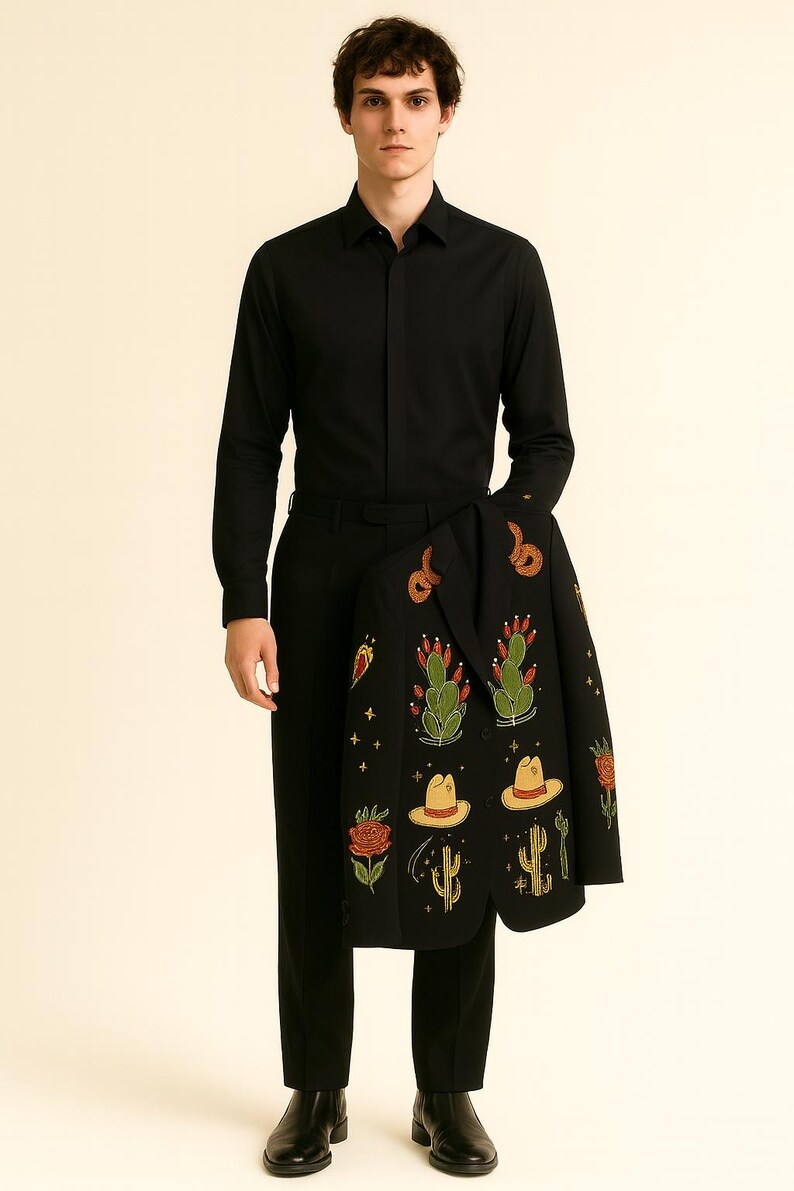 May include: A person wearing a black button-down shirt and black pants, holding a black jacket. The jacket is decorated with colorful embroidered cacti, hats, and flowers. The overall theme is Western-inspired apparel.