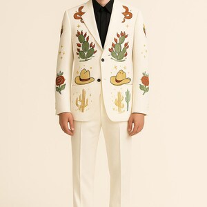 May include: Ivory suit with embroidered desert-themed designs. The blazer features cacti, cowboy hats, and roses in green, yellow, and red. The suit is paired with a black dress shirt and black shoes. The suit is a unique fashion statement.