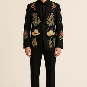 May include: Black suit with embroidered desert-themed designs. The blazer features cacti, cowboy hats, and roses in green, red, and tan. The suit is paired with a black dress shirt and black dress pants.