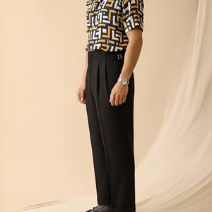 Puede incluir: Una camisa de manga corta con estampado geom&eacute;trico en azul marino, amarillo y blanco se combina con pantalones negros plisados. El conjunto se completa con mocasines de cuero marr&oacute;n y un reloj de pulsera plateado. El estilo general es cl&aacute;sico y sofisticado.
