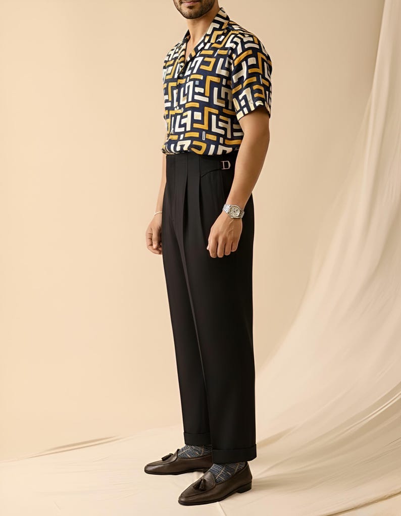 Puede incluir: Una camisa de manga corta con estampado geom&eacute;trico en azul marino, amarillo y blanco se combina con pantalones negros plisados. El conjunto se completa con mocasines de cuero marr&oacute;n y un reloj de pulsera plateado. El estilo general es cl&aacute;sico y sofisticado.