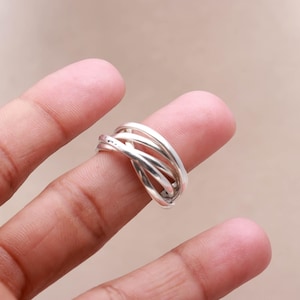 Op de afbeelding: Een zilverkleurige ring met een geweven ontwerp. De ring heeft meerdere banden die in elkaar grijpen en een unieke en stijlvolle uitstraling creëren. De ring wordt op een vinger getoond tegen een neutrale achtergrond.