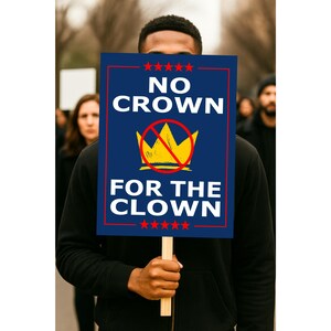 May include: A person holding a sign with the text "NO CROWN FOR THE CLOWN" in white letters on a navy blue background. The sign has a red border and a yellow crown with a red slash through it. The person is wearing a black hoodie.