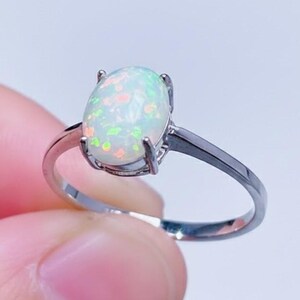 Könnte beinhalten: Ein silberner Ring mit einem ovalen Opal-Edelstein. Der Opal zeigt eine Mischung aus Farben, darunter Weiß, Grün und Orange. Der Ring hat ein schlichtes, poliertes Silberdesign, das den Edelstein hervorhebt.