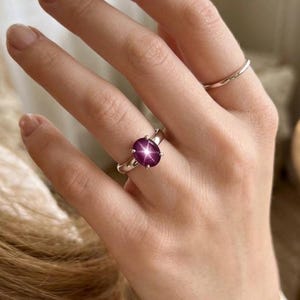 Puede incluir: Un anillo de plata con una gran gema de rub&iacute; estrella de talla ovalada. El rub&iacute; es de color p&uacute;rpura rojizo intenso con un efecto de estrella de seis rayos. Tambi&eacute;n se ve una segunda banda de plata lisa. El anillo es una joya.