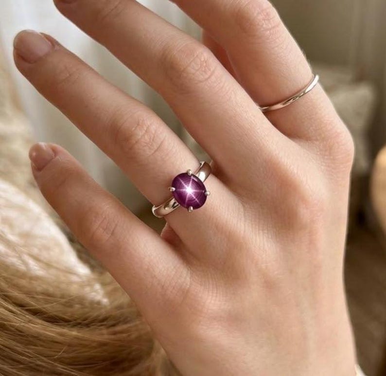 Puede incluir: Un anillo de plata con una gran gema de rub&iacute; estrella de talla ovalada. El rub&iacute; es de color p&uacute;rpura rojizo intenso con un efecto de estrella de seis rayos. Tambi&eacute;n se ve una segunda banda de plata lisa. El anillo es una joya.