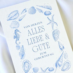 Könnte beinhalten: Eine weiße Keramik-Tasse mit schwarzem Henkel und dem Text "But First, Coffee" in schwarzer, handschriftlicher Schrift. Die Tasse steht auf einer weißen Oberfläche.