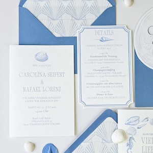 Può includere: Invito di nozze a tema spiaggia. Include biglietti d'invito, buste con motivi a conchiglia e una scheda dettagli. La combinazione di colori è blu e bianco, con illustrazioni di conchiglie e cavallucci marini. È incluso anche un sigillo di cera.
