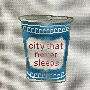 May include: Needlepoint art of a blue coffee cup with a gray lid. The cup features the phrase "city that never sleeps" in red letters. The design is stitched on a white canvas.