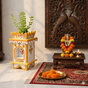 Puede incluir: Un templo de madera pintado de blanco y amarillo, con una planta en su interior. El templo está sobre un suelo blanco. Una pequeña mesa de madera sostiene una estatua adornada con flores, una vela encendida y un plato de latón con flores.