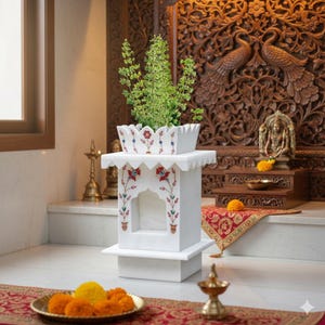 May include: A white marble altar with floral inlay, holding a green plant. The altar has a decorative arch design and sits on a square base. The background features carved wooden panels and religious items.