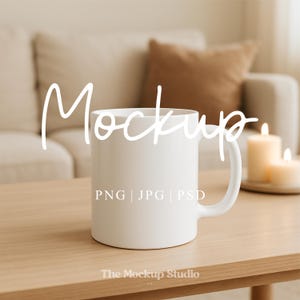 Könnte beinhalten: Eine weiße Keramiktasse mit gebogenem Henkel steht auf einem hellen Holztisch. Das Wort "Mockup" ist in Schreibschrift über der Tasse geschrieben. Darunter stehen die Worte "PNG | JPG | PSD". The Mockup Studio UK steht unten.