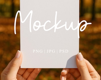 May include: A white rectangular card held by hands, with the word "Mockup" in cursive script. Below, it reads "PNG | JPG | PSD". The background features blurred autumn foliage.
