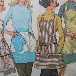 May include: Four women wearing different styles of aprons. The aprons are in various colors and patterns, including striped, floral, and solid colors. The women are all smiling and looking at the camera.