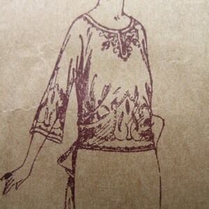 May include: A sepia-toned illustration of a long-sleeved top with intricate floral embroidery around the neckline, sleeves, and waist. The garment appears to be made of a lightweight fabric, with a flowing silhouette. The drawing style suggests a vintage or antique aesthetic.