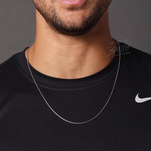 May include: A man wearing a black t-shirt with a white Nike swoosh logo. He is wearing a silver chain necklace.