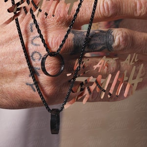 May include: Two black chain necklaces with circular pendant charms. The necklaces are worn by a person with a tattoo on their hand.