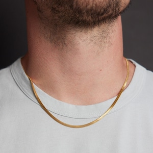 May include: A gold chain necklace on a person wearing a light blue t-shirt.