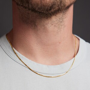 May include: A gold chain necklace on a person wearing a light blue t-shirt.