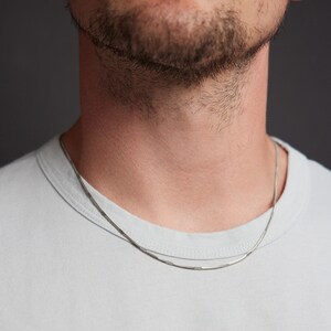 May include: A silver chain necklace on a person wearing a light blue t-shirt.