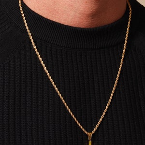 May include: A gold-colored cross pendant necklace. The cross hangs from a matching gold rope chain. The necklace is displayed against a black background.