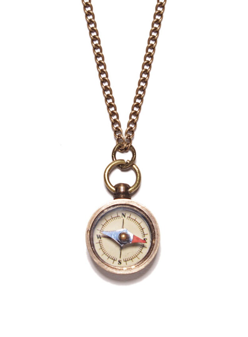 May include: A gold compass necklace with a chain. The compass face is white with black markings and a red and blue needle.