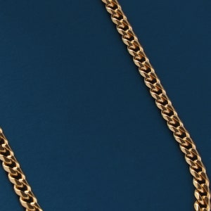 May include: A gold chain necklace with a curb link style on a blue background.