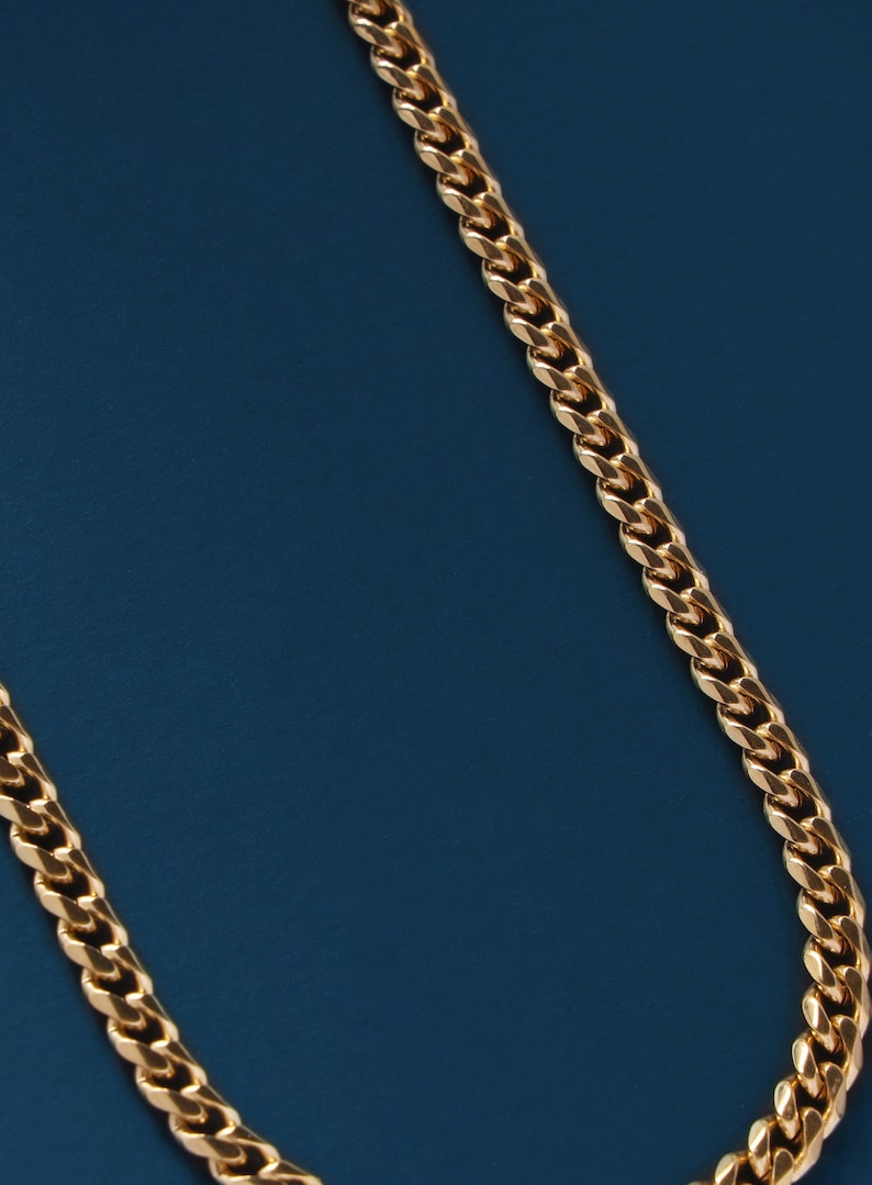 May include: A gold chain necklace with a curb link style on a blue background.